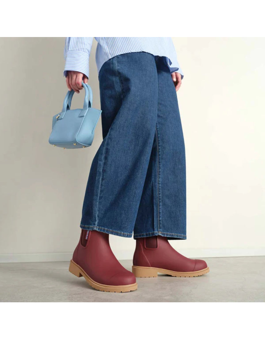 Brick red Merry People Bobbi gumboots worn by a model, showcasing stylish waterproof rubber footwear for rainy days.
