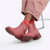 Merry People Bobbi Gumboot in clay color, stylish waterproof rubber boots with a textured sole, sitting outdoors.