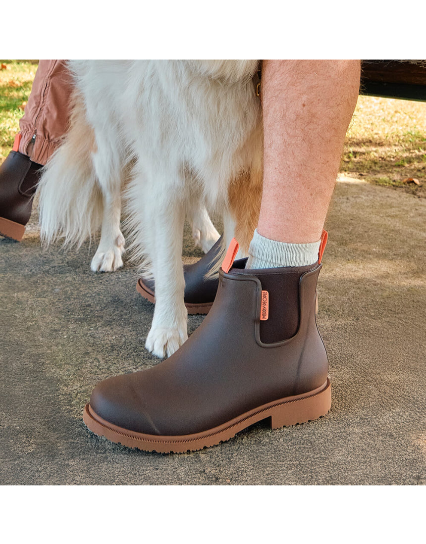 Merry People Bobbi Gumboots in mocha color, stylish waterproof rain boots shown outdoors with greenery in the background.