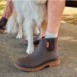 Merry People Bobbi Gumboots in mocha color, stylish waterproof rain boots shown outdoors with greenery in the background.