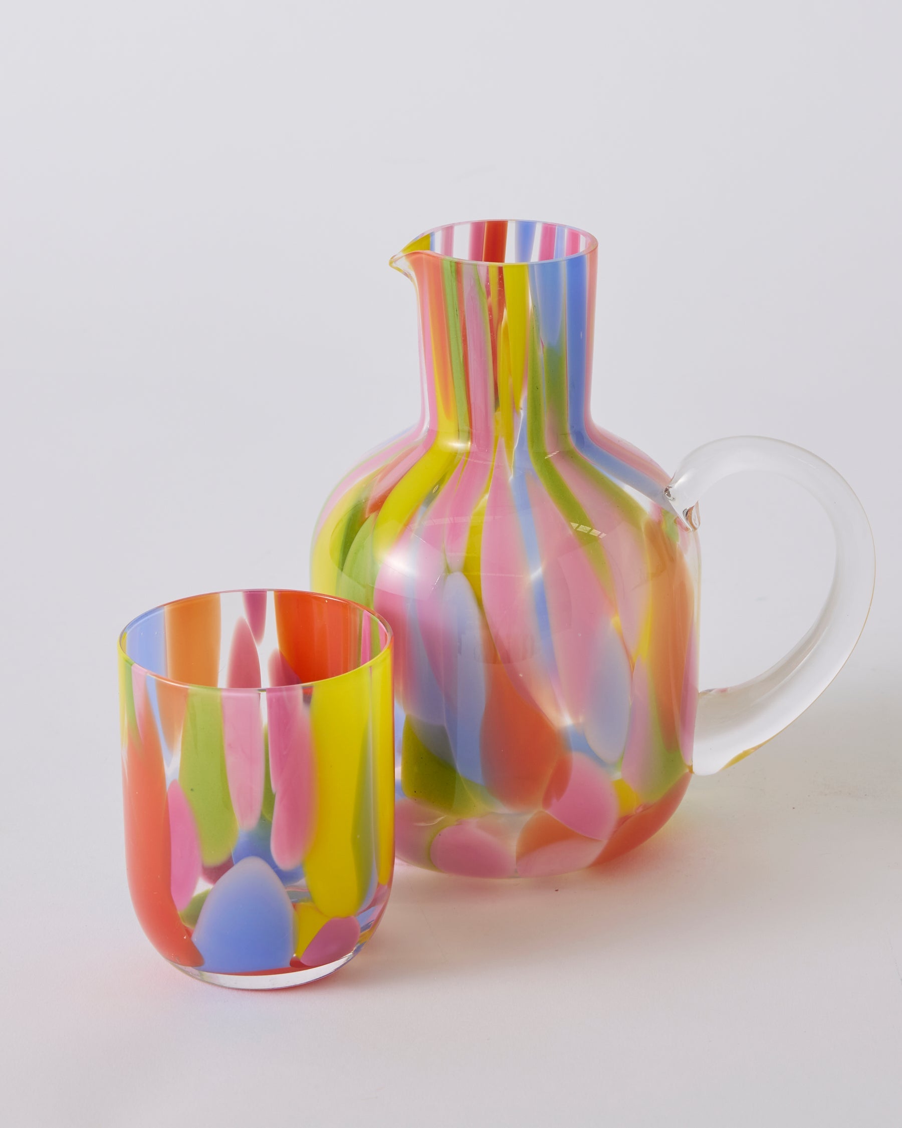 Kip & Co Festiva carafe and glass set on a table with vibrant, colorful patterns, showcasing stylish drinkware design.