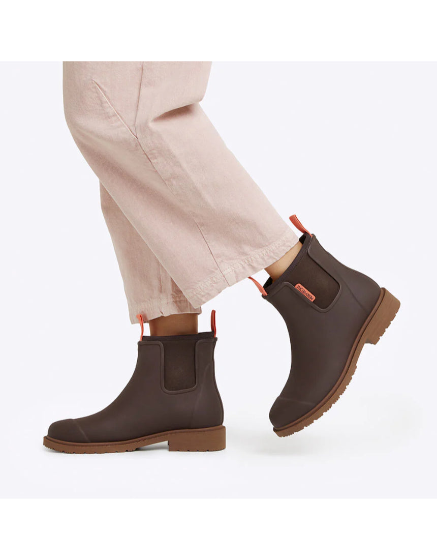 Merry People Bobbi Mocha gumboots worn by a person walking outdoors, showing stylish waterproof footwear on a natural trail.