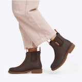 Merry People Bobbi Mocha gumboots worn by a person walking outdoors, showing stylish waterproof footwear on a natural trail.