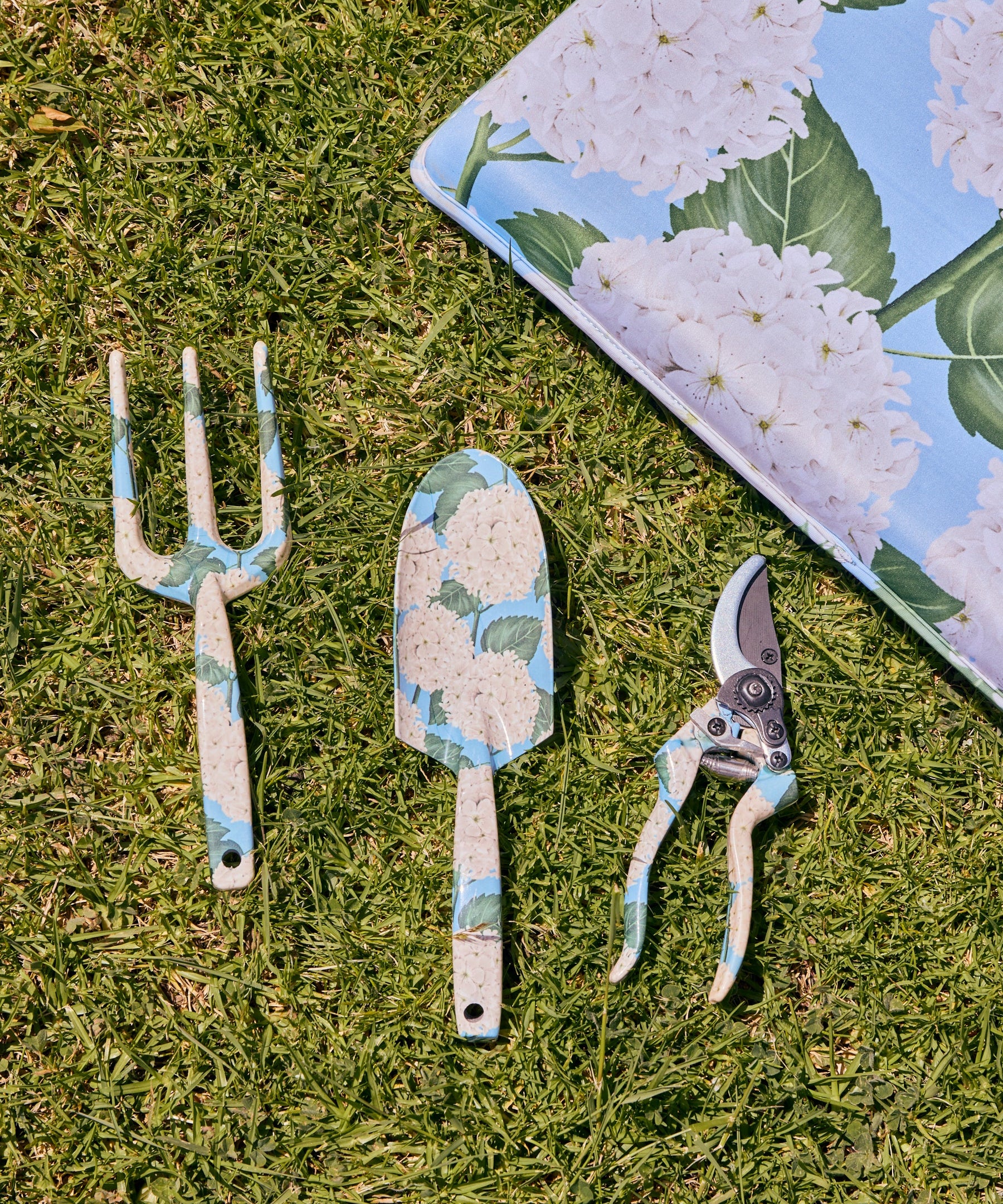 Kip & Co hydrangea blue garden tools and gloves set with trowel, pruners, and protective gardening gloves on a garden background
