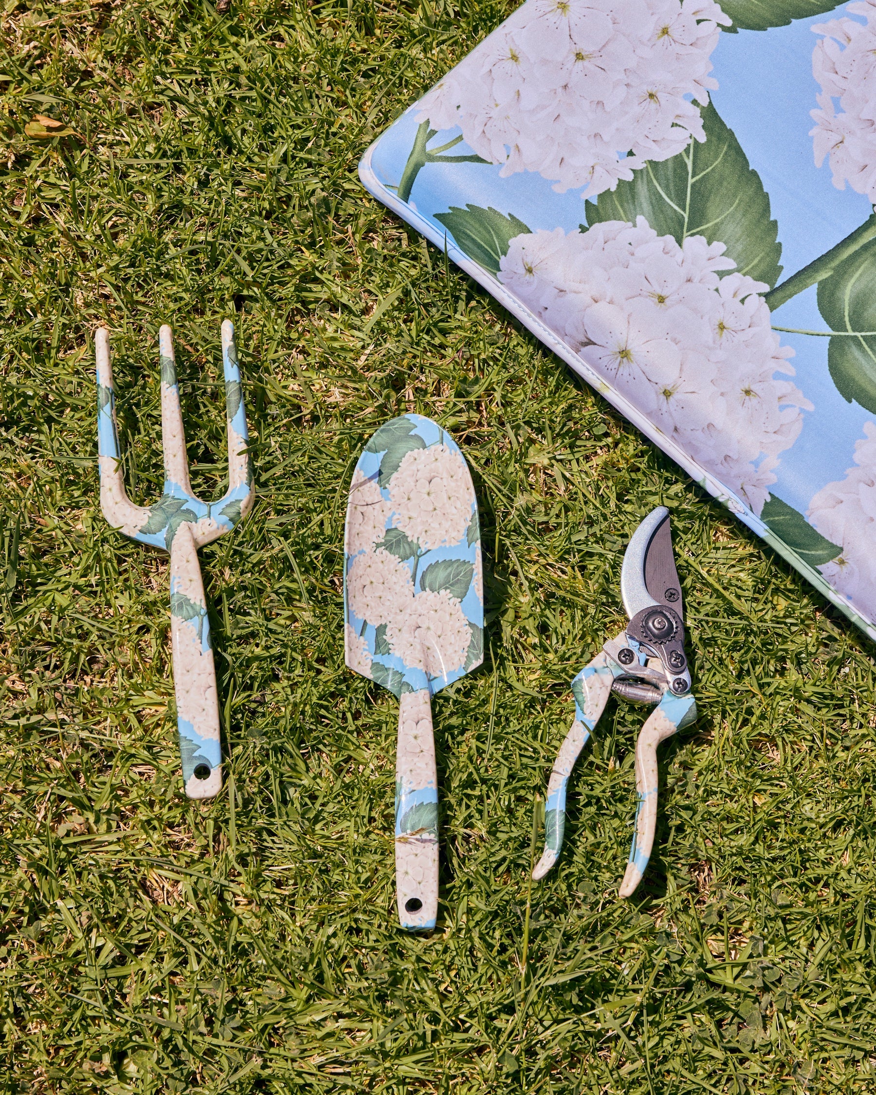 Kip & Co hydrangea blue garden tools and gloves set with trowel, pruners, and protective gardening gloves on a garden background