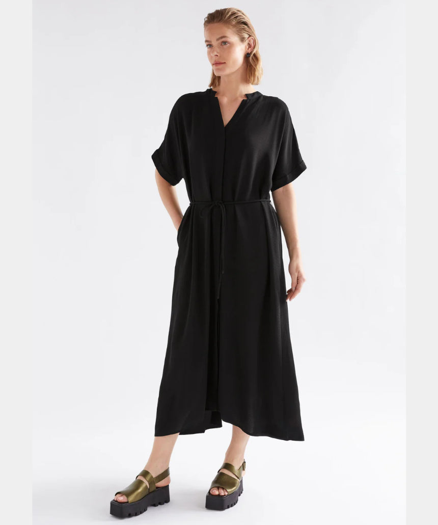 Black Elk Omia Shirt Dress hanging on a wooden hanger, showcasing its relaxed fit and classic shirt dress style.