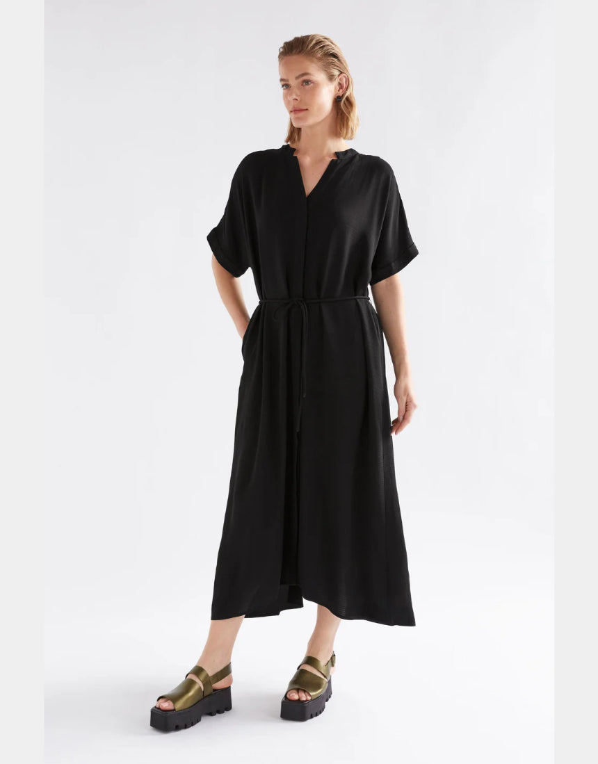 Black Elk Omia Shirt Dress hanging on a wooden hanger, showcasing its relaxed fit and classic shirt dress style.