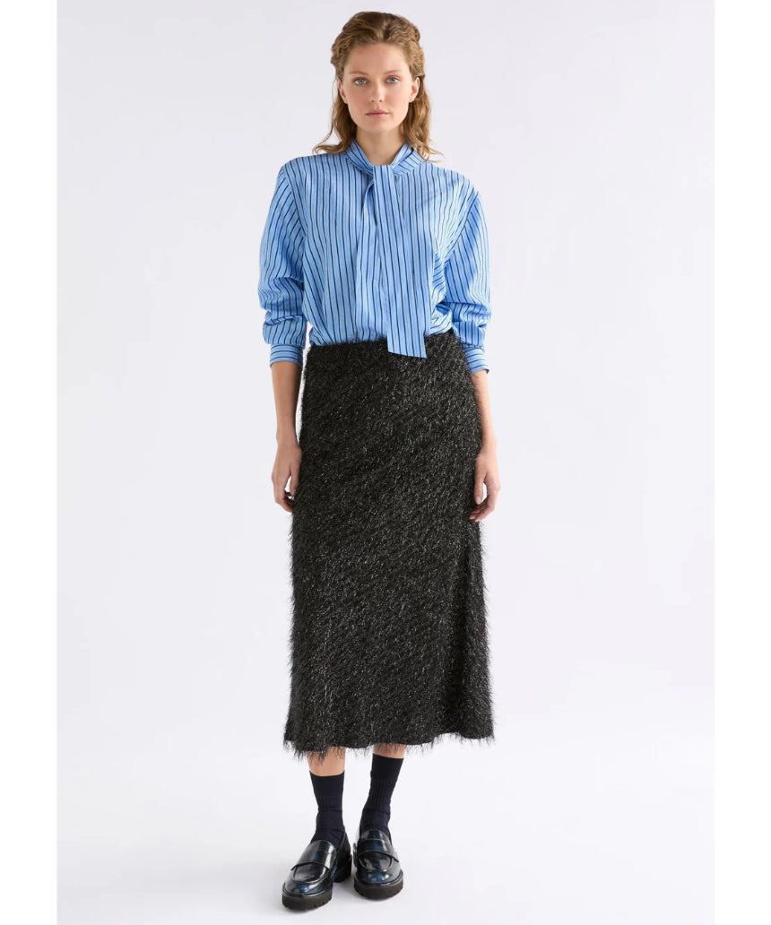 Black Elk Ilta Skirt, stylish clothing with a flowy design, shown on a model in a natural sitting pose.