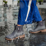Merry People Bobbi gumboots in charcoal color, stylish waterproof footwear, shown outdoors with a person wearing casual clothing.