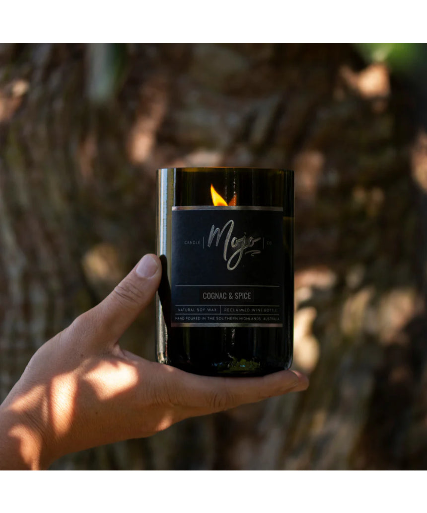 Mojo Candle Co. Cognac & Spice Black Label candle in a dark glass jar with a lit wick, emitting a warm, spicy glow.