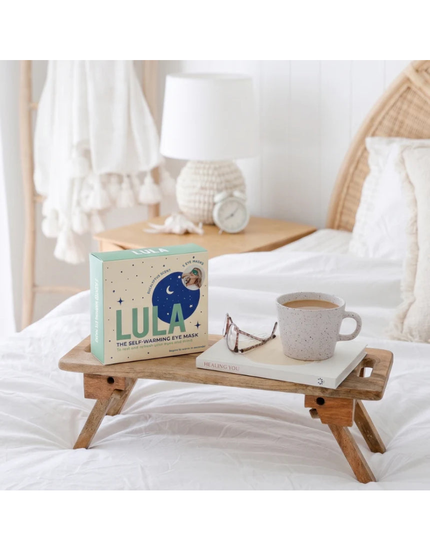 Lula self-warming eucalyptus and tea tree eye mask lying flat on a white surface, showing soft fabric and adjustable strap.