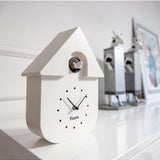 White Fisura cuckoo clock with traditional design, featuring a wooden case and a small cuckoo door on the front.