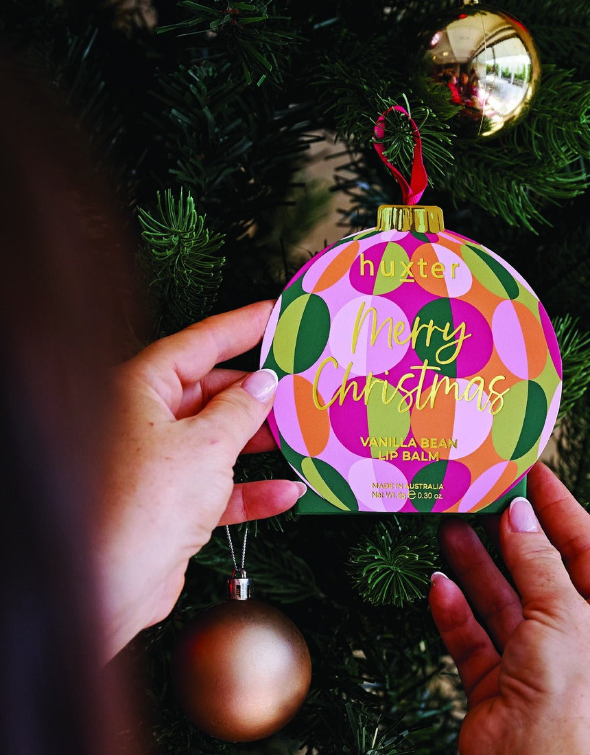 Hands holding Huxter Green Hanging Lip Balm on a Christmas tree