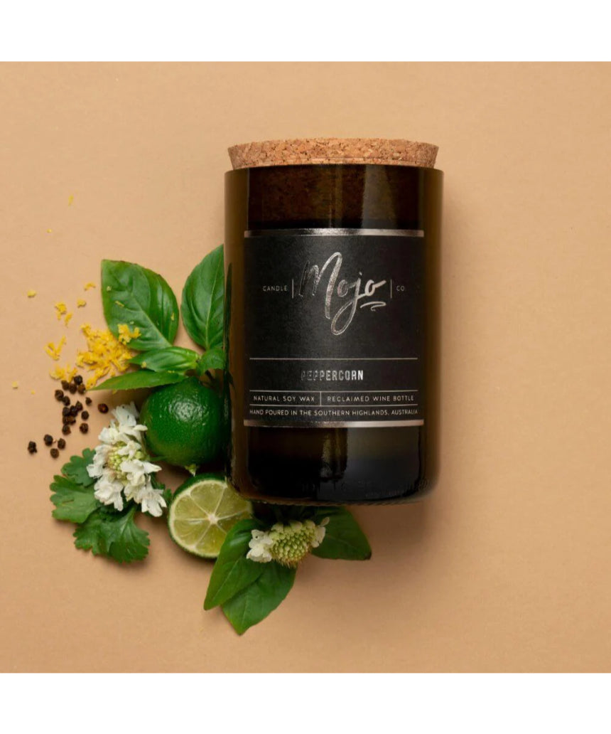 Flatlay of Mojo Candle Co. Peppercorn Black Label candle with peppercorns and a wine bottle for a cozy, aromatic ambiance.