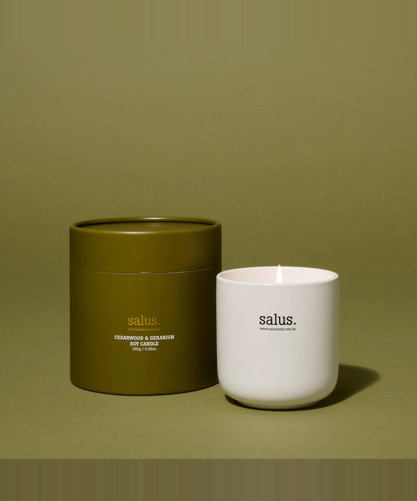 Salus Cedarwood and Geranium soy candle in a glass jar, placed on a wooden table with a cozy, relaxing ambiance.