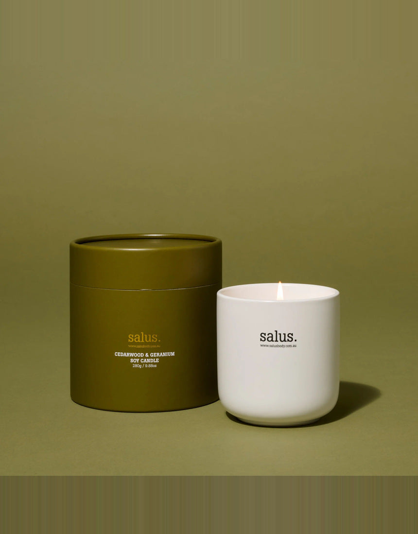 Salus Cedarwood and Geranium soy candle in a glass jar, placed on a wooden table with a cozy, relaxing ambiance.