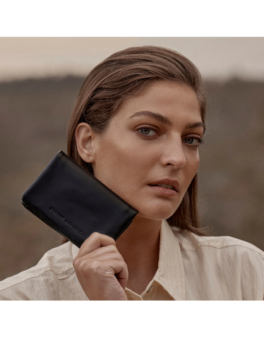 Black Status Anxiety Is Now Better Wallet with multiple card slots and sleek design, shown in a lifestyle setting.
