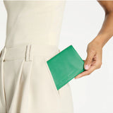 Status Anxiety Is Now Better Wallet in emerald green, showing a slim leather wallet with multiple card slots and a sleek design.