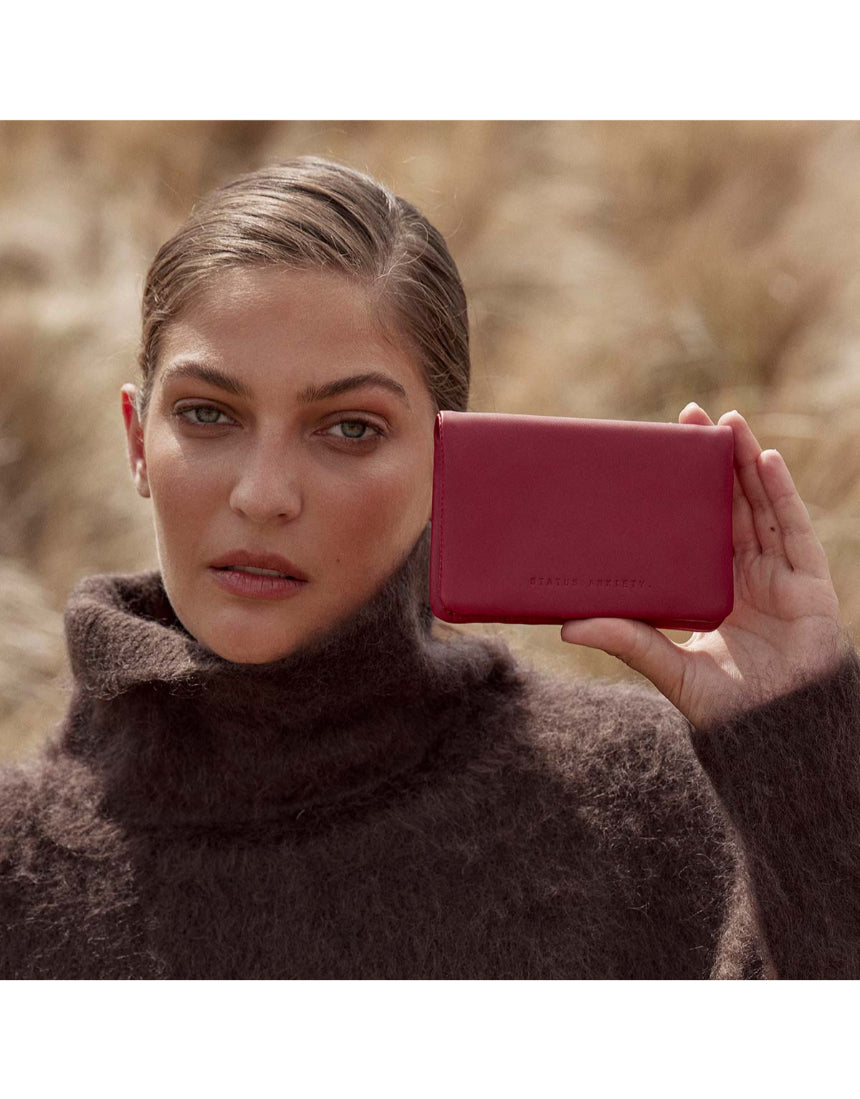 Status Anxiety Is Now Better Wallet in Rouge, featuring a sleek leather design with multiple card slots and a compact silhouette.