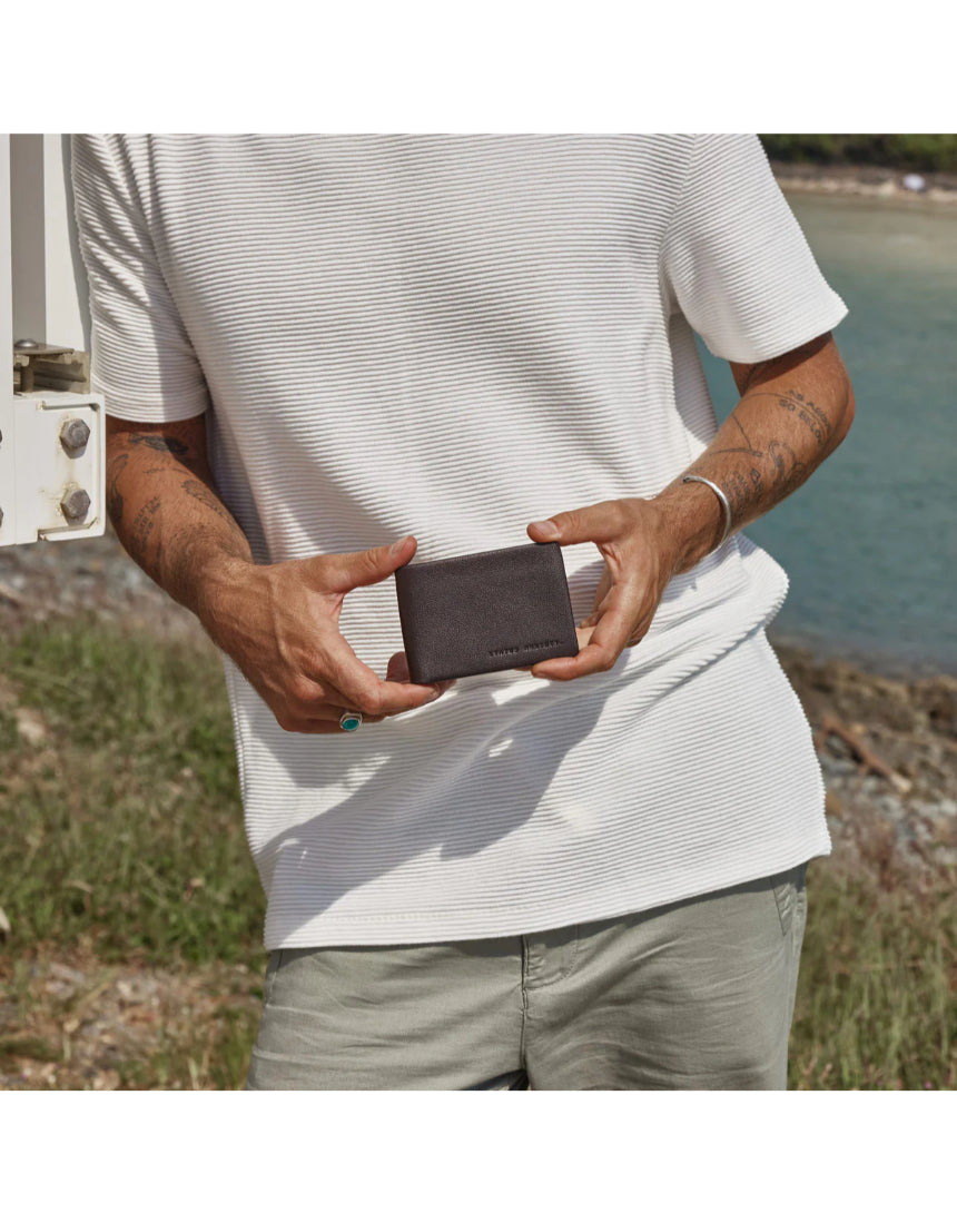 Chocolate Status Anxiety Jonah Wallet with multiple card slots and sleek design, shown in lifestyle setting.