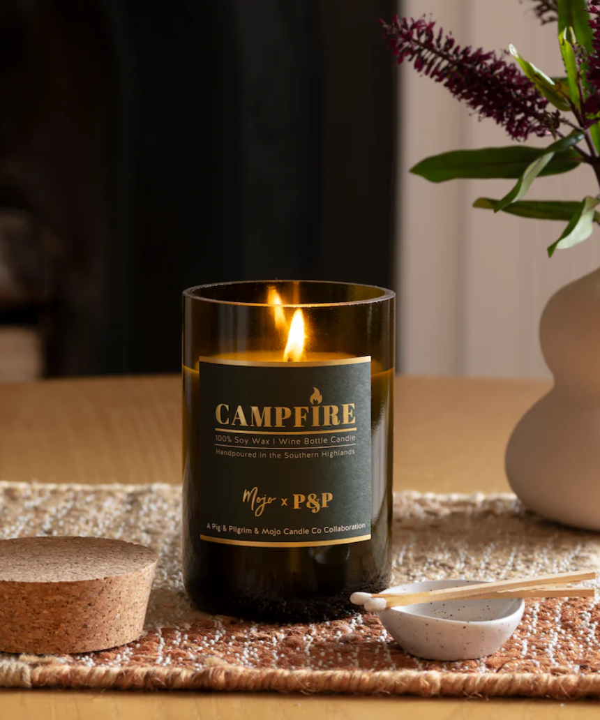 Mojo Candle Co. campfire scented candle in a glass jar, with a warm glow and wooden wick for cozy ambiance.