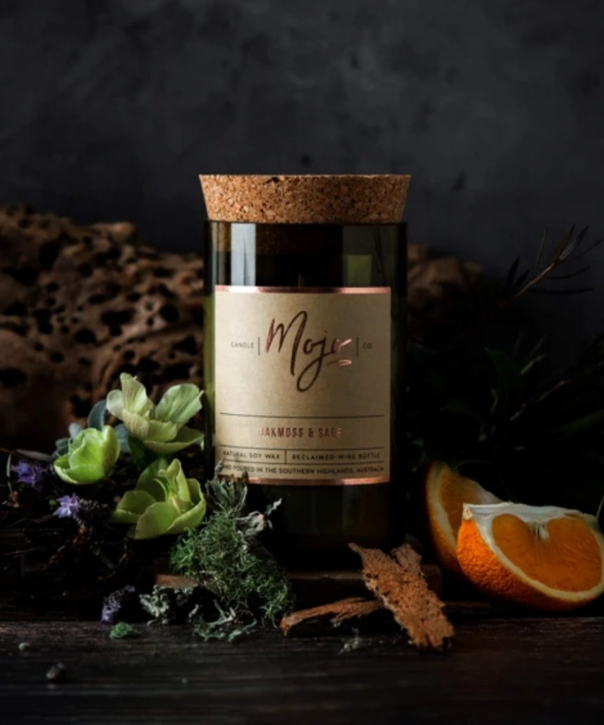Mojo Candle Co. oakmoss and sage scented candle with a glass jar and wooden lid, showcasing natural botanical elements.