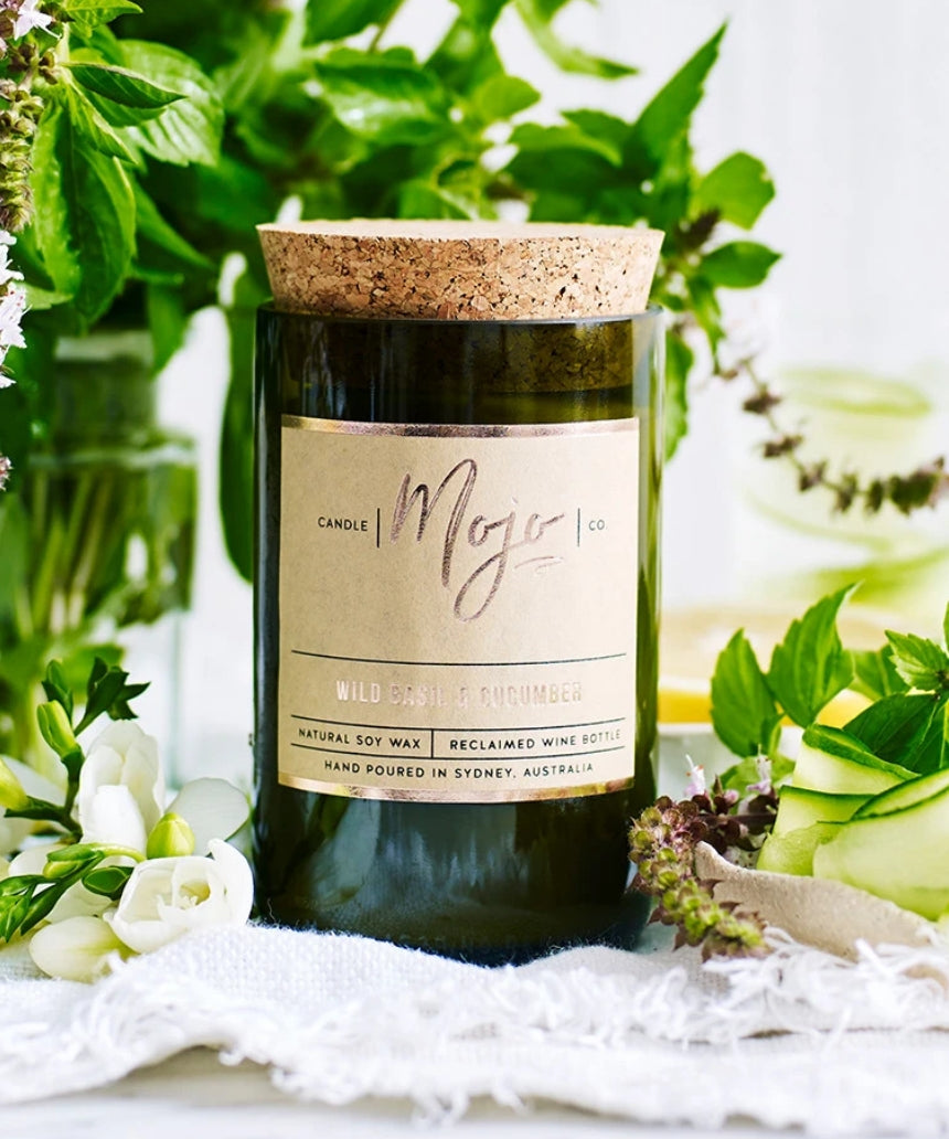 Wild Basil and Cucumber scented candle by Mojo Candle Co., featuring a sleek glass jar with a lit wick and fresh botanical design.