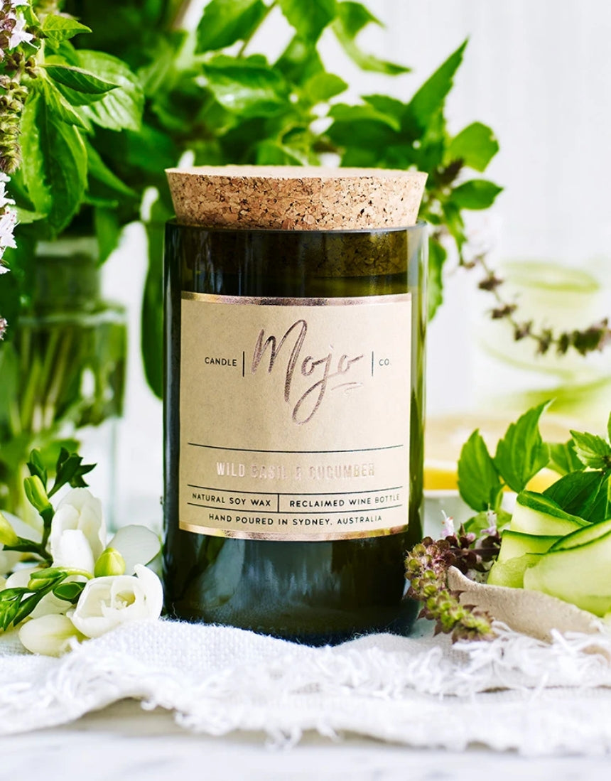 Wild Basil and Cucumber scented candle by Mojo Candle Co., featuring a sleek glass jar with a lit wick and fresh botanical design.