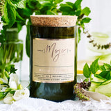 Wild Basil and Cucumber scented candle by Mojo Candle Co., featuring a sleek glass jar with a lit wick and fresh botanical design.